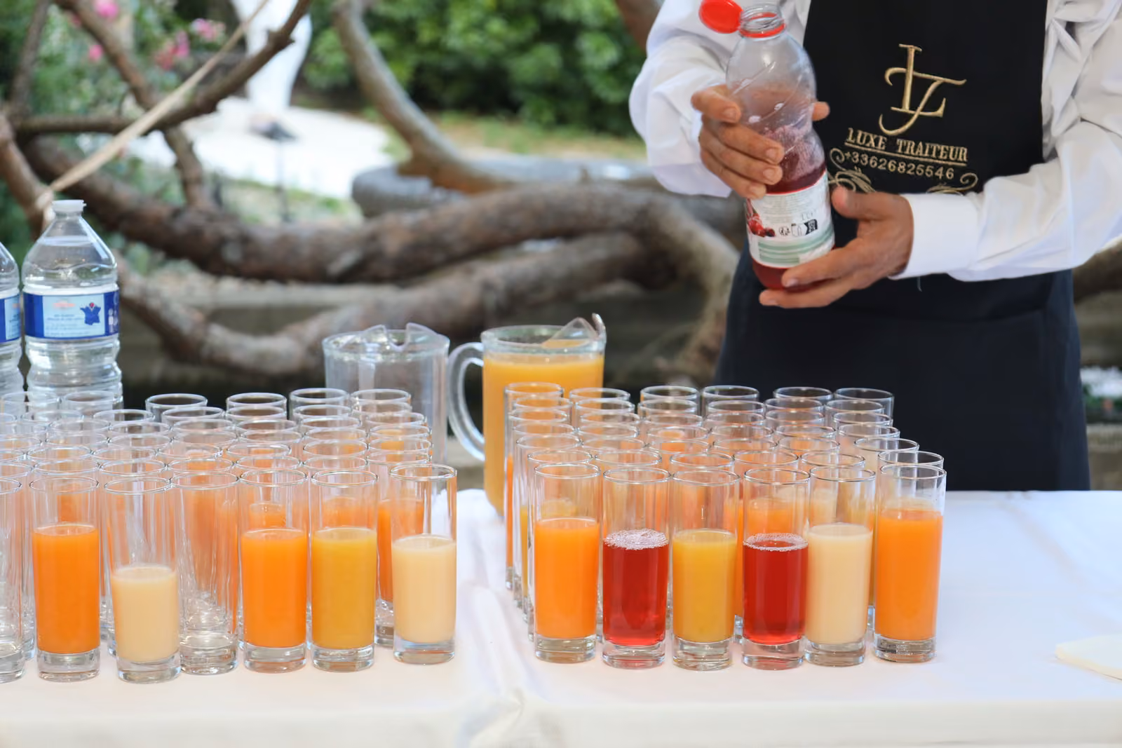 Serveur en tablier noir versant des jus et cocktails sans alcool dans des verres alignés sur un buffet