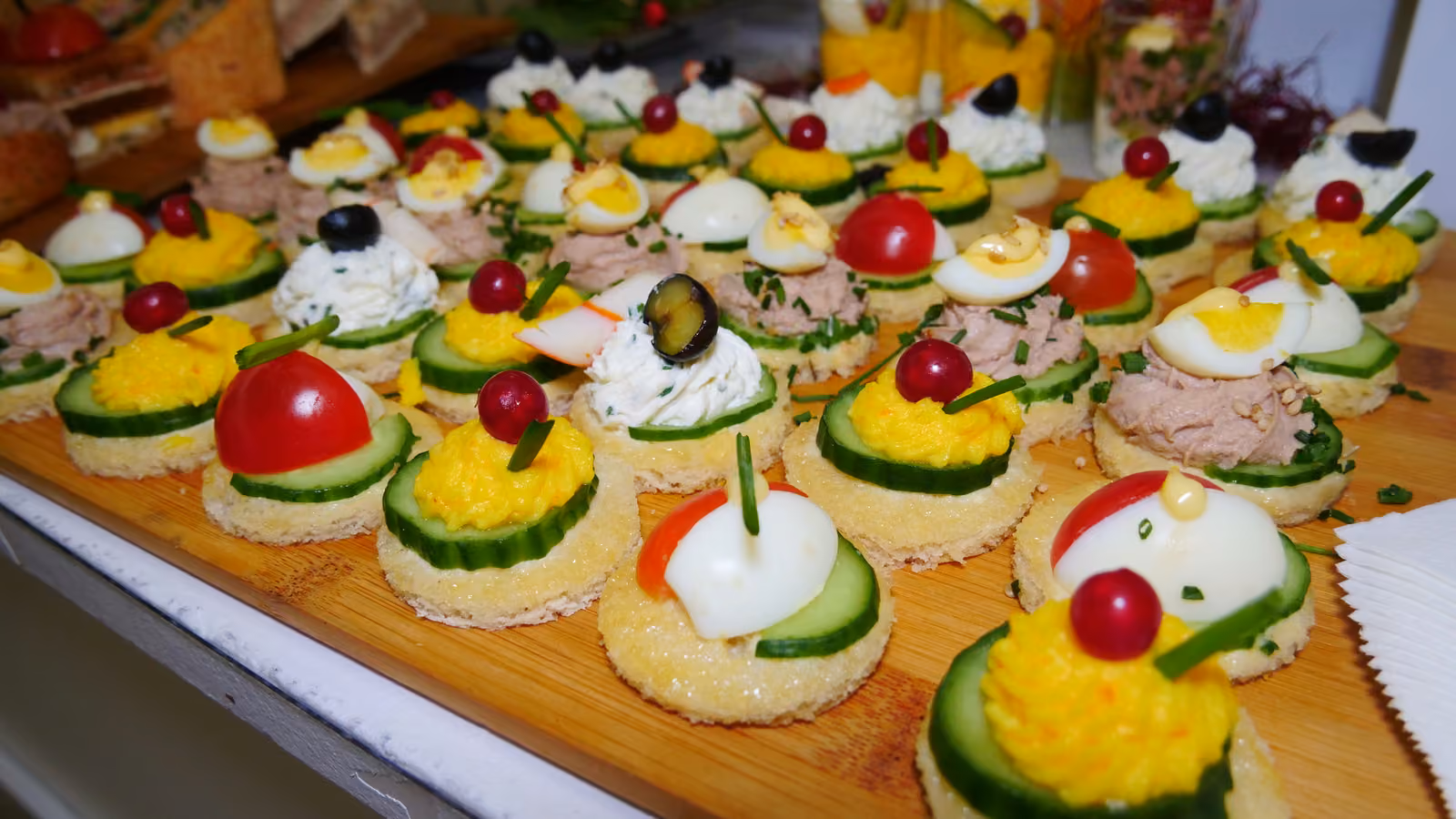 Canapés variés sur un plateau en bois : œuf, thon, tomate cerise, concombre et olive