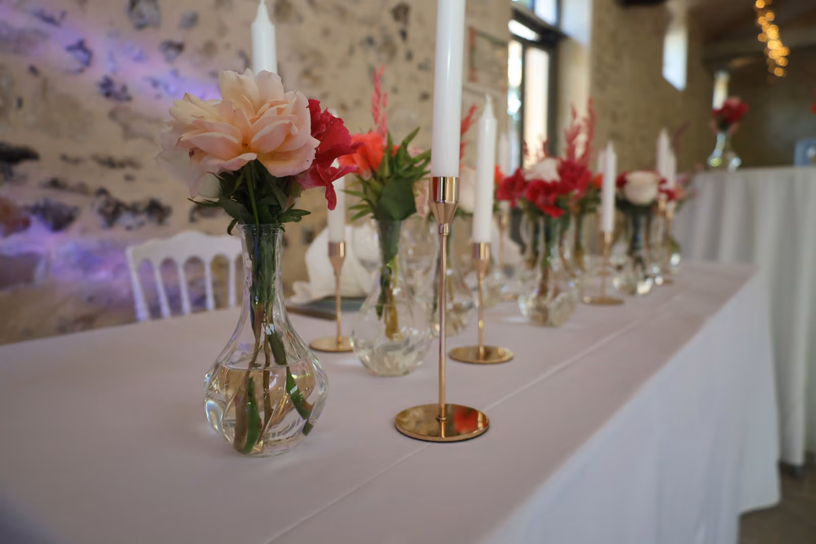 Détail d'une table de mariage : pivoine pêche en vase boule, chandelier doré et bougie blanche