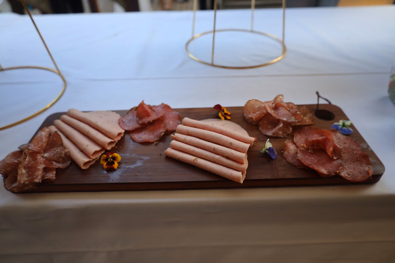 Planche en bois de charcuterie : jambon blanc, saucisson et rosette, fleurs comestibles