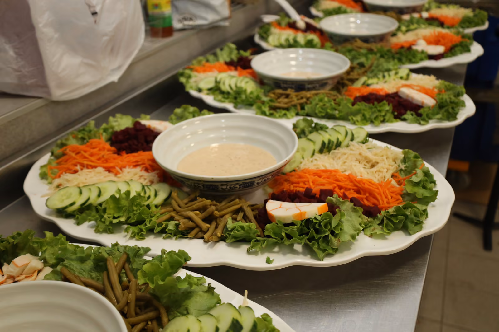 Grands plats de crudités, carottes râpées, betteraves et sauce préparés en cuisine avant le service