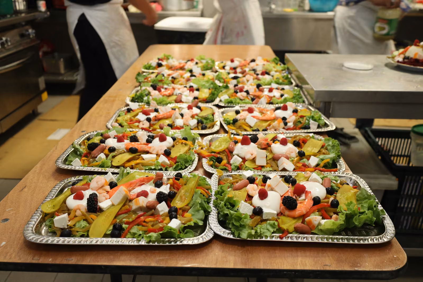 Rangées de barquettes de salades composées aux crevettes, feta et fruits préparées en cuisine