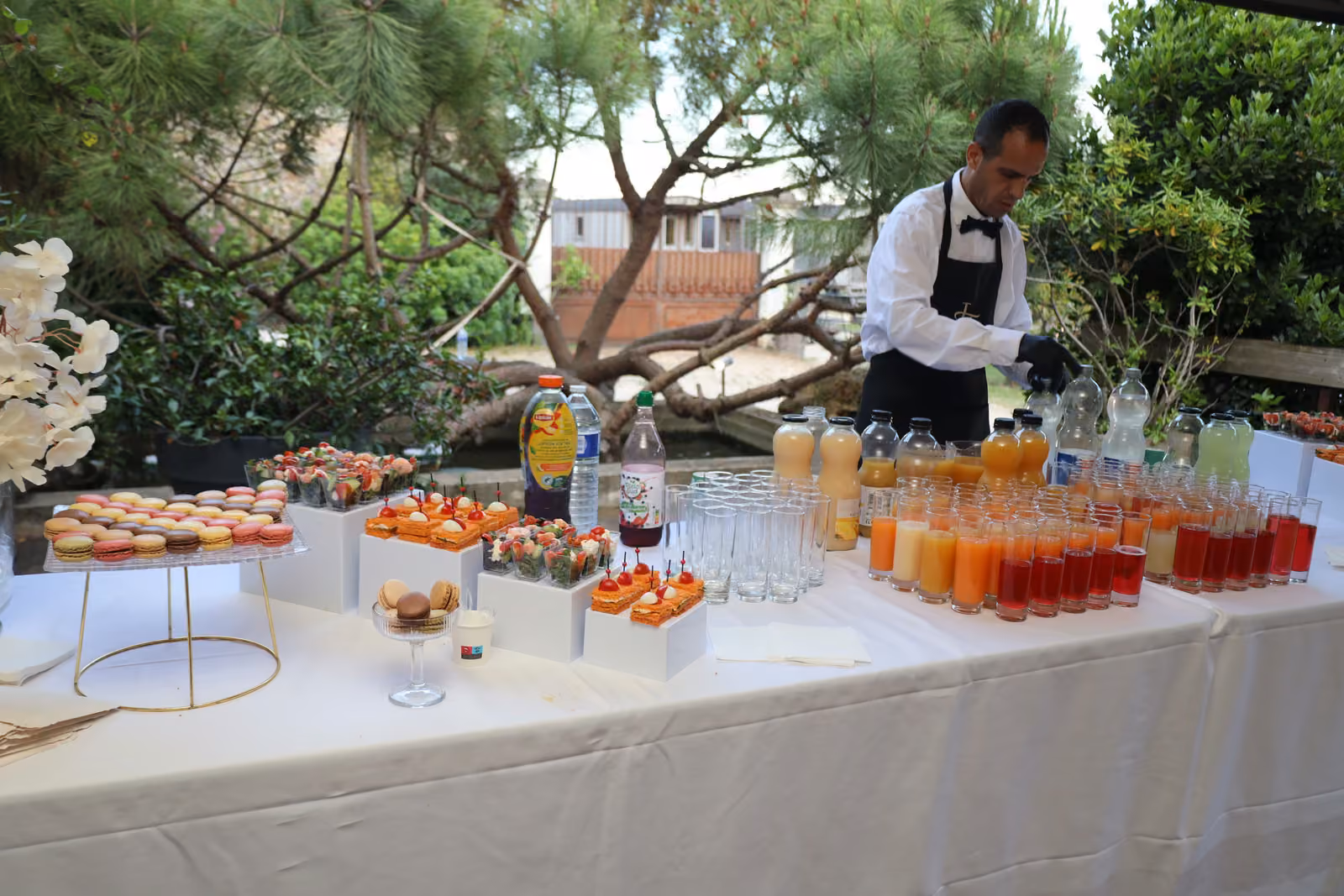 Serveur en nœud papillon préparant des jus frais au bout d'un buffet installé en jardin