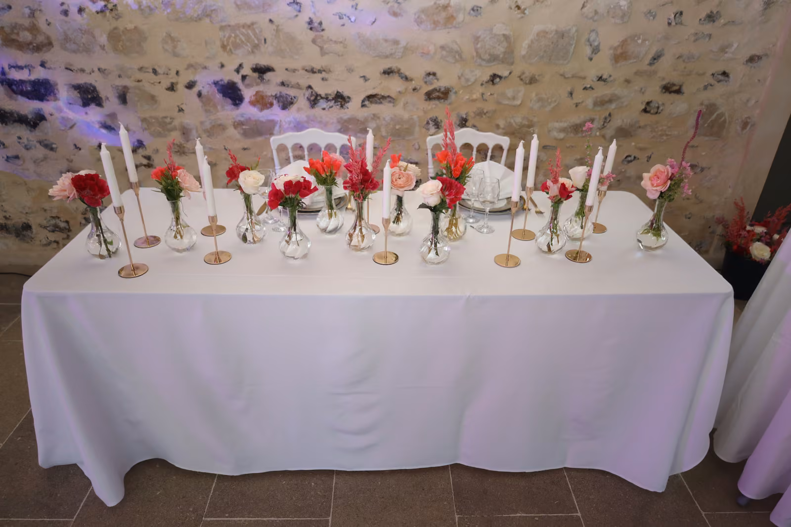 Table d'honneur de mariage nappée de blanc, soliflores rouges et roses, chandeliers dorés et bougies