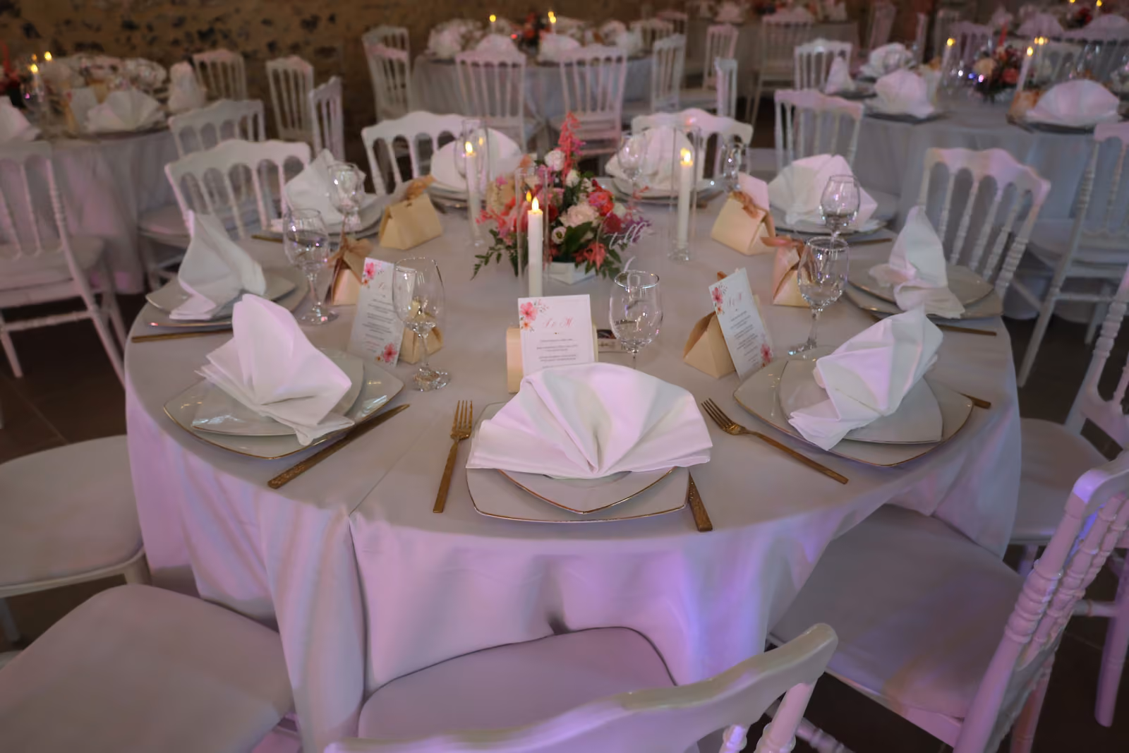 Table ronde de mariage dressée : serviettes pliées en éventail, assiettes, couverts dorés et bouquet central